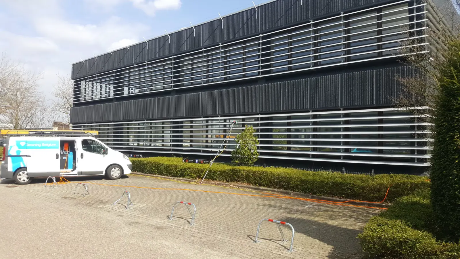 Bedrijfswagen van Diamond Cleaning Belgium voor een kantoorgebouw met aluminium gevellamellen, met de telescoopsteel klaar voor gebruik