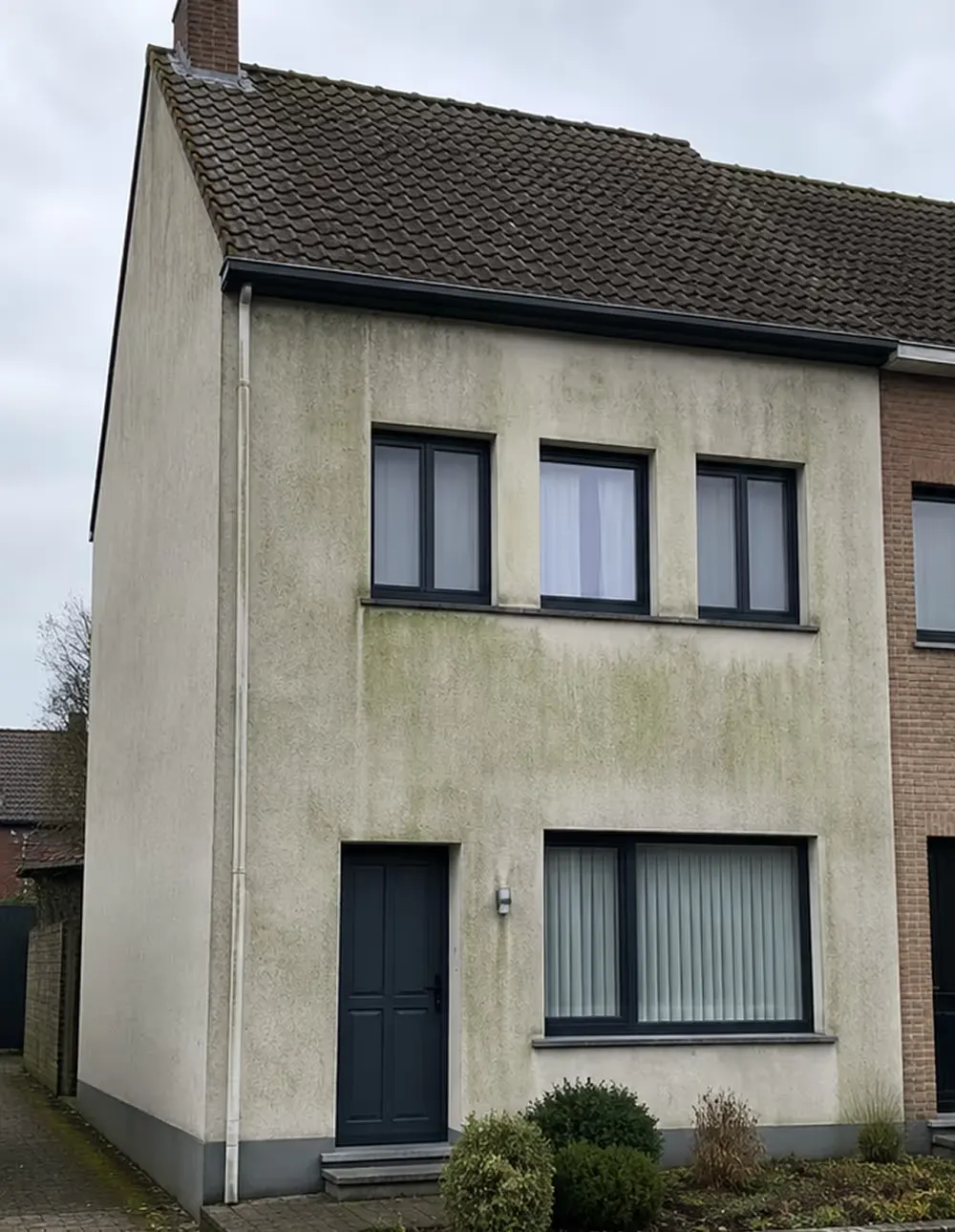 Vervuilde crepi gevel met groene aanslag en donkere strepen voor de reiniging