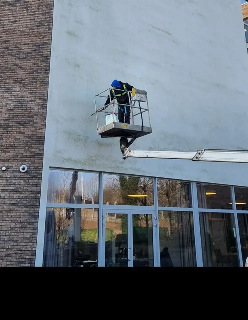 Medewerker reinigt een witte crepigevel vanuit een hoogwerker