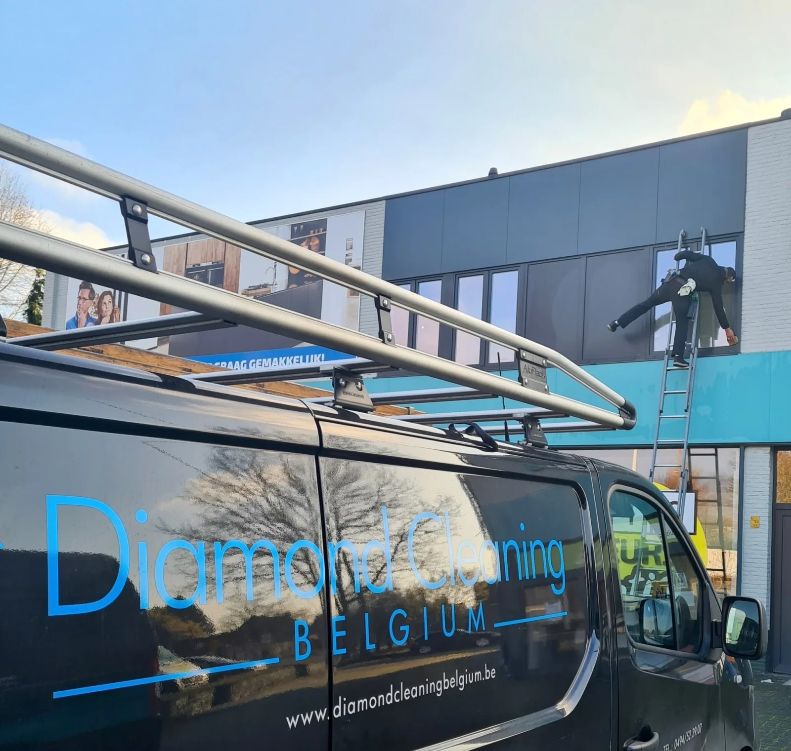 Bedrijfswagen van Diamond Cleaning Belgium voor een winkelpand, waar een medewerker op een ladder de ramen van de eerste verdieping wast.