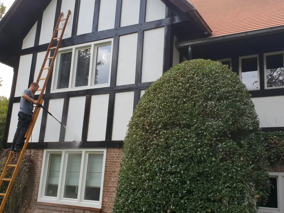Medewerker reinigt de gepleisterde gevel van een woning vanaf een ladder