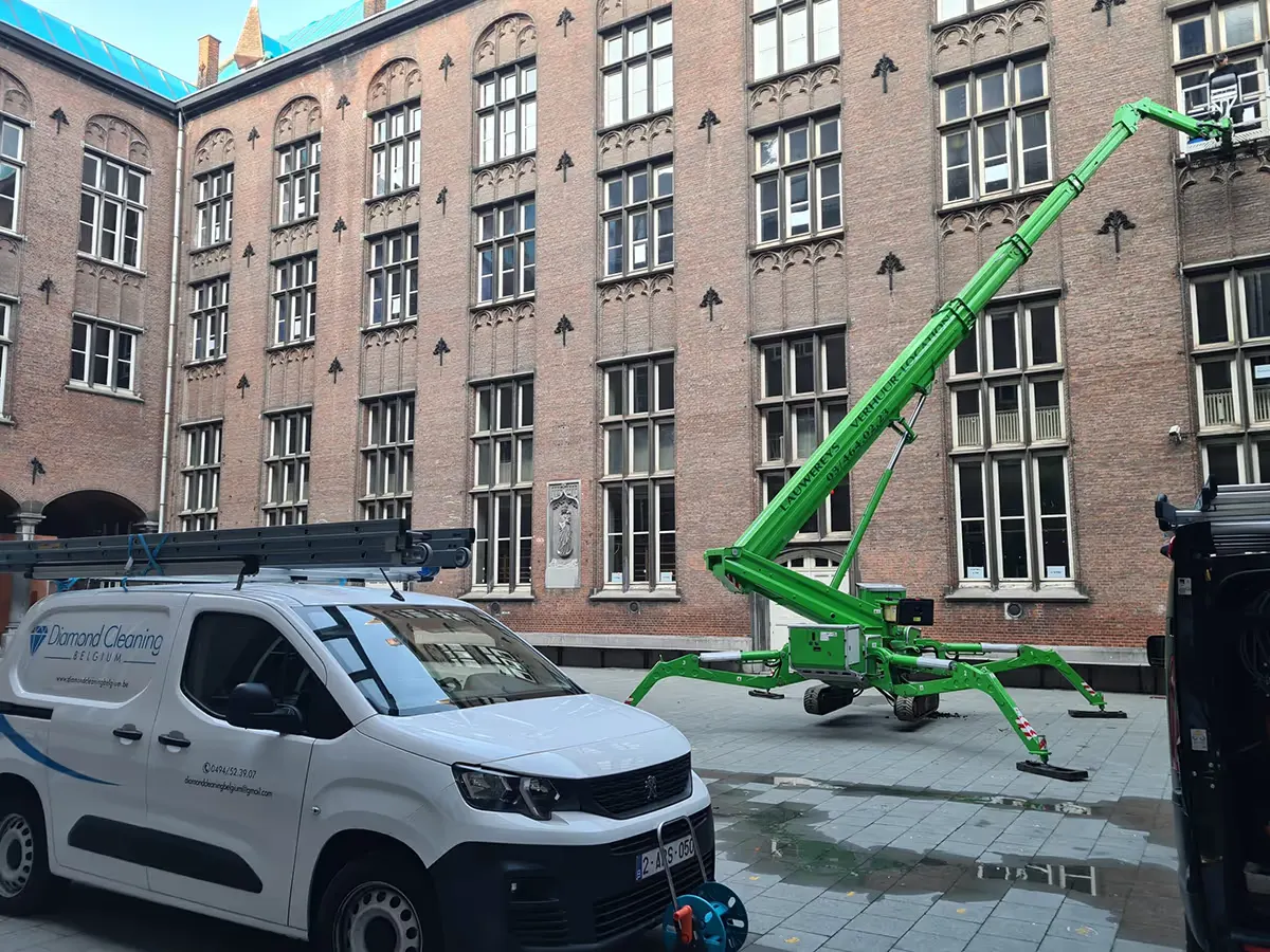 Hoogwerker en bedrijfswagen van Diamond Cleaning Belgium op de binnenplaats van een schoolgebouw in Lier