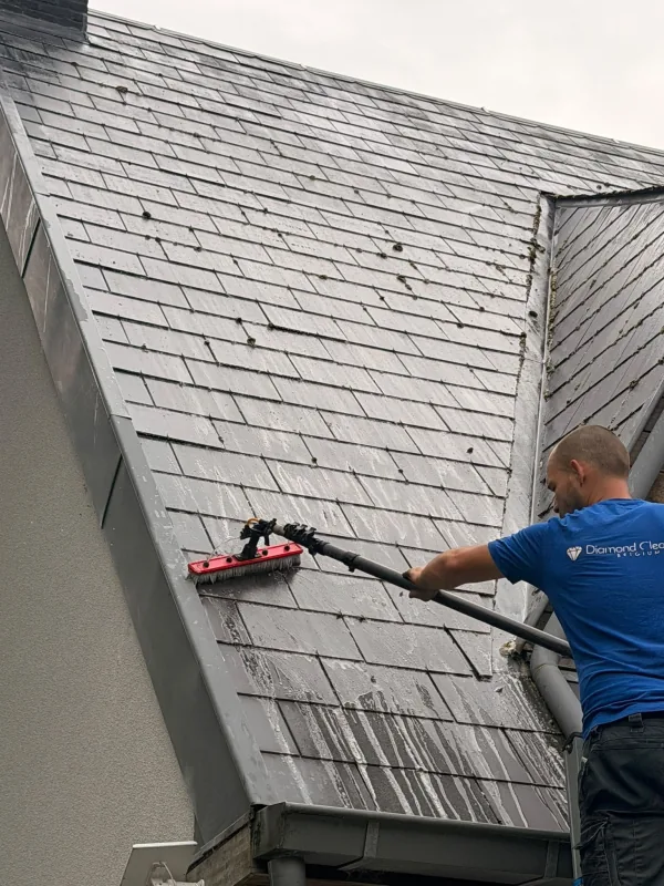 Medewerker van Diamond Cleaning borstelt een leien dak met een telescoopsteel