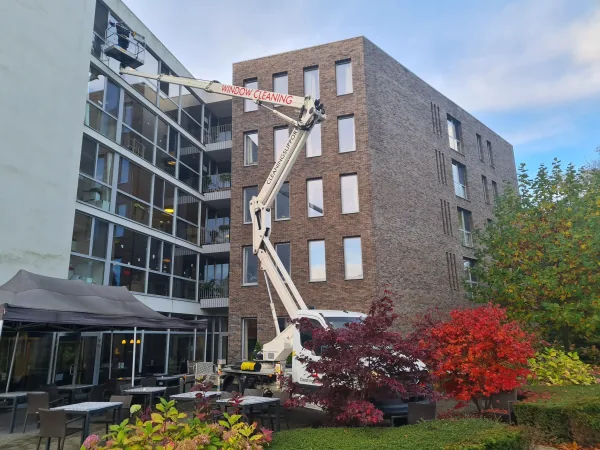Hoogwerker aan een bakstenen appartementsgebouw tijdens de ramenreiniging