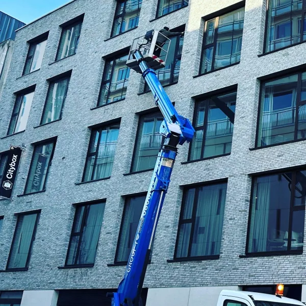 Blauwe hoogwerker aan een gevel met veel ramen tijdens het wassen van de ramen op hoogte