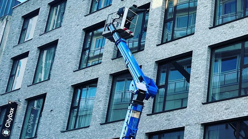 Medewerker reinigt ramen van een appartementsgebouw vanuit een blauwe hoogwerker