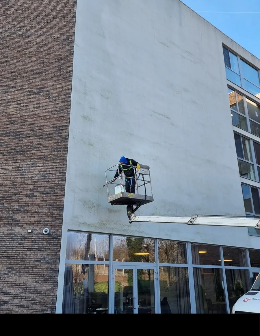 Medewerker reinigt een witte crepigevel vanuit een hoogwerker