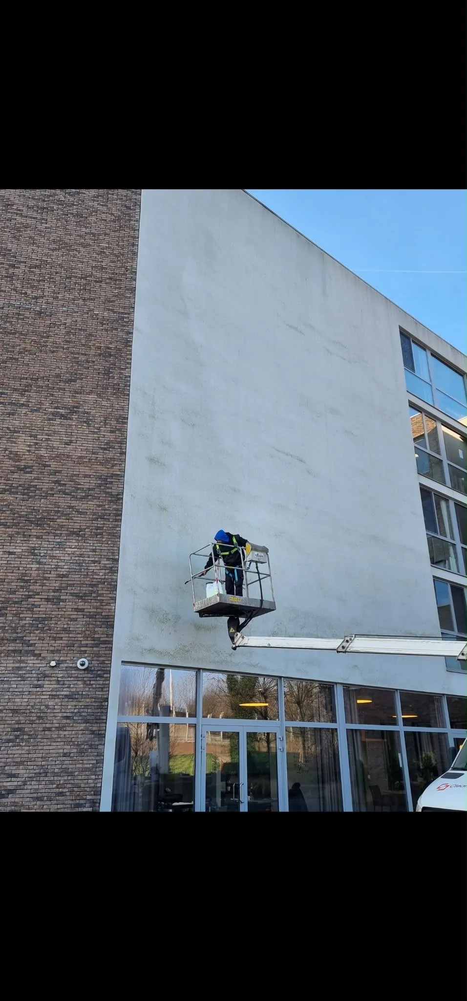 Gevelreiniging vanuit een hoogwerker langs een witte gevel