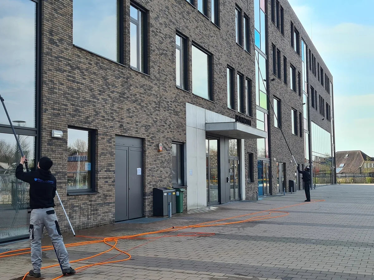 Twee ramenwassers met telescoopstelen bij een kantoorgebouw