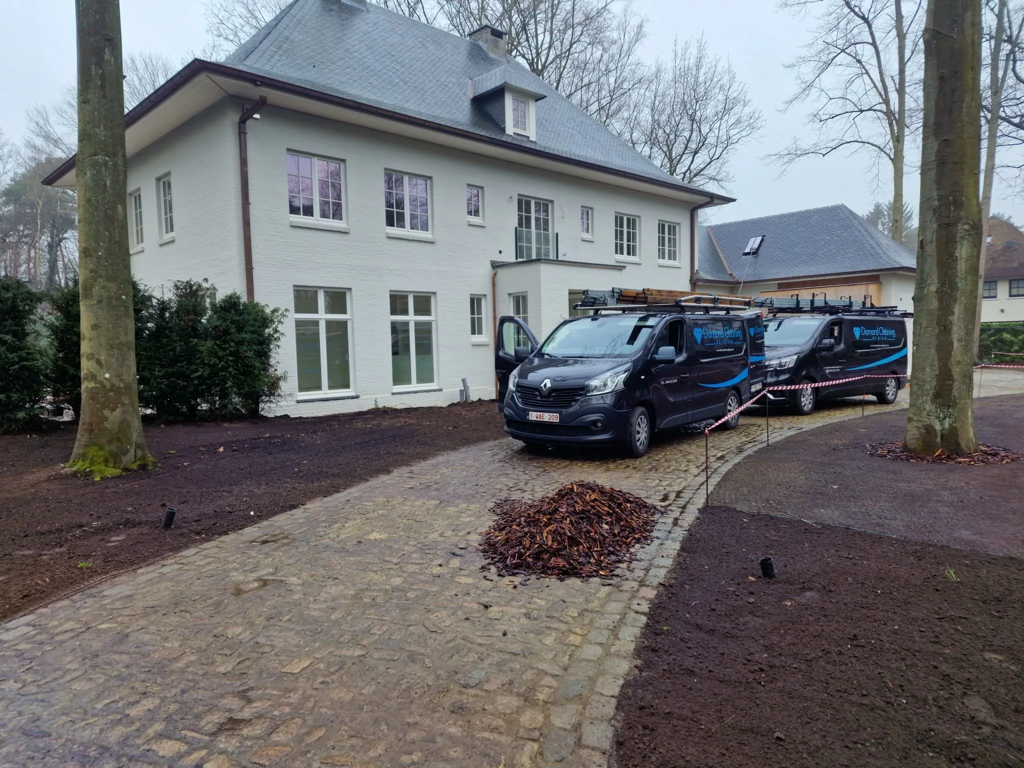 Twee bestelwagens van Diamond Cleaning Belgium op de oprit van een villa