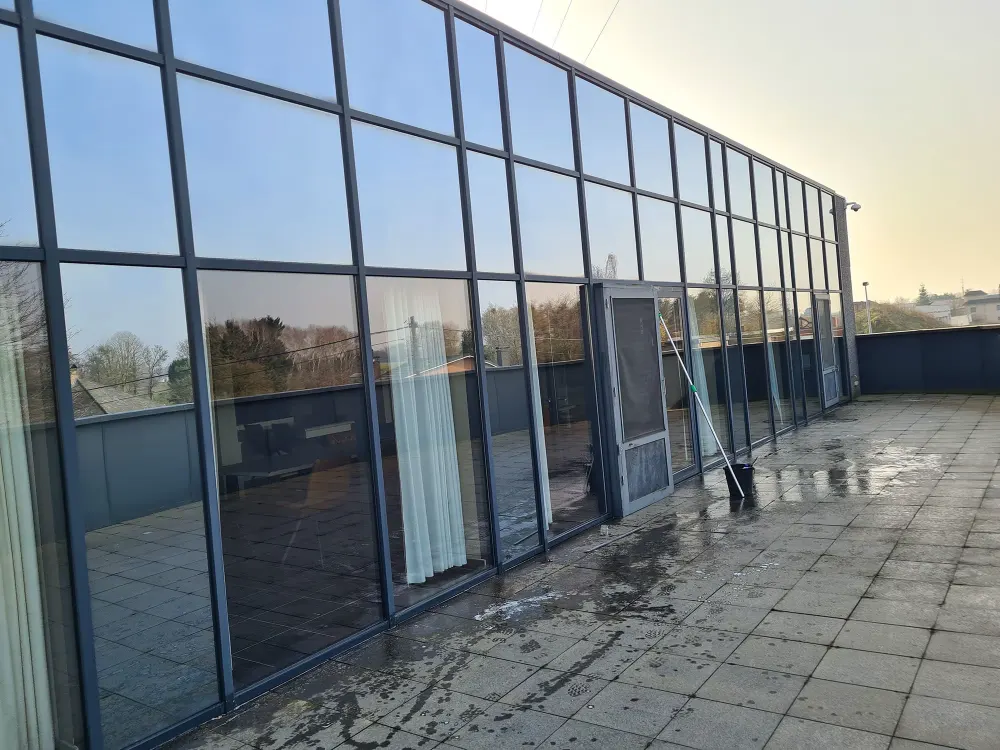 Pas gereinigde glaspartij van een bedrijfsgebouw, met telescoopsteel en emmer op het dakterras
